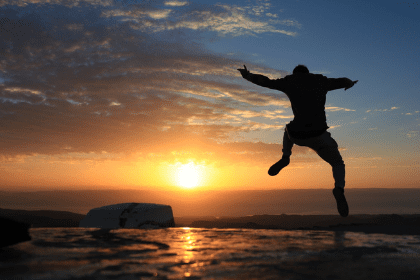 man-springt-in-lucht-bij-het-strand-zondsondergang